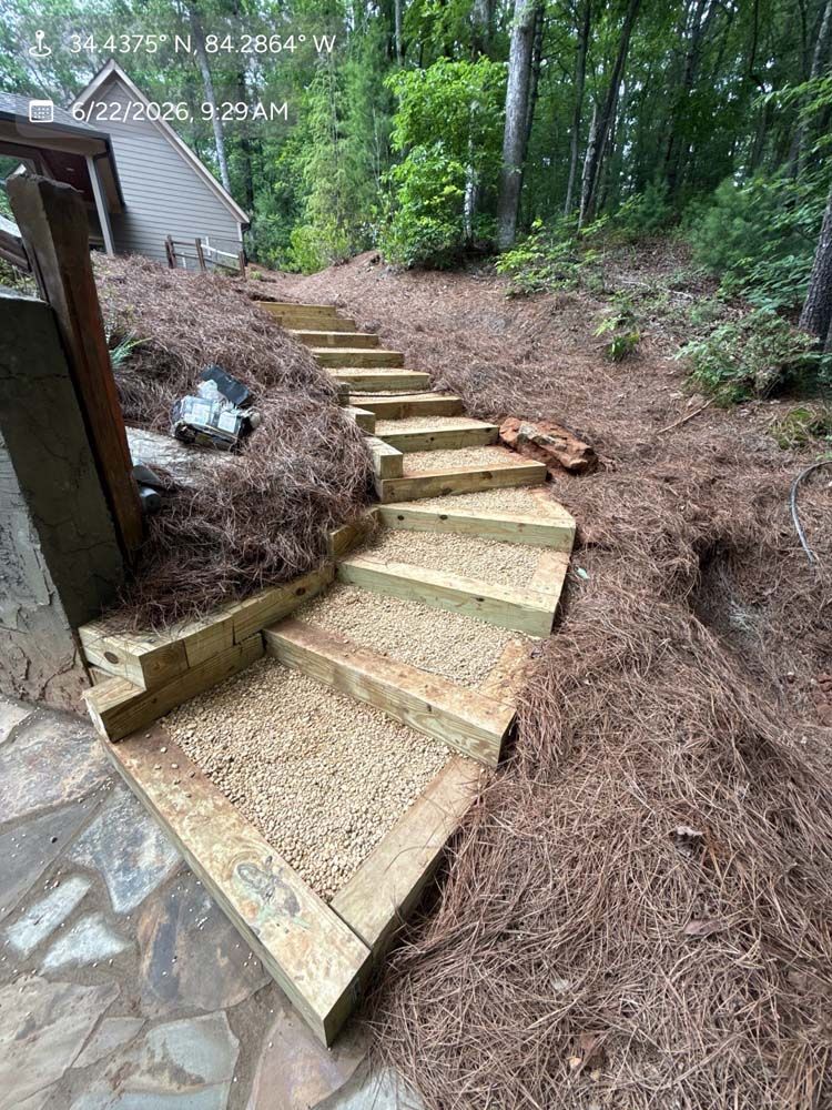 Composite stair run with black cable railing descending from an elevated deck past a dry-stack stone foundation into landscaped beds