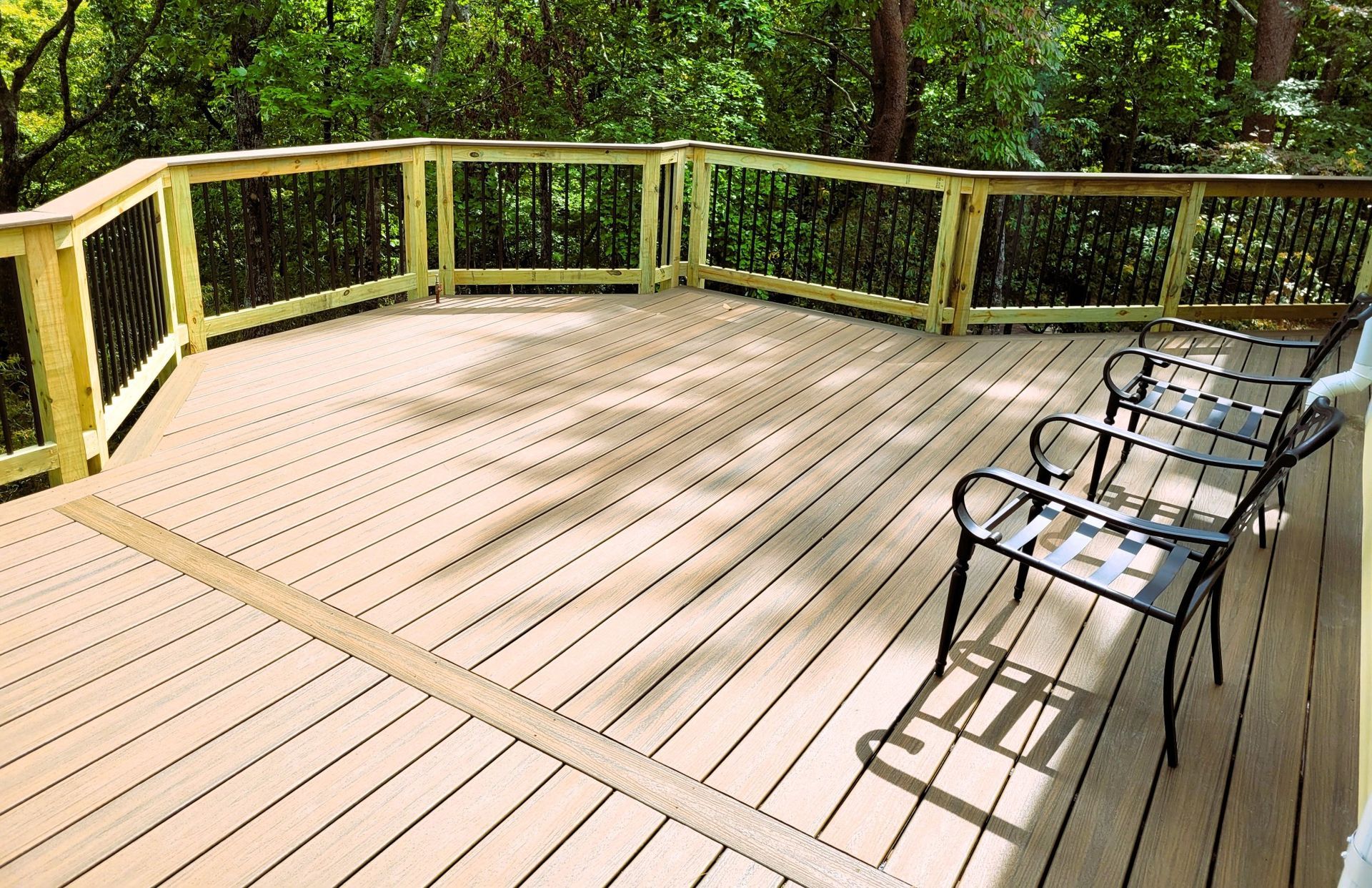 Multi-level composite deck in tan with wood railings, black metal balusters, and patio chairs overlooking woods
