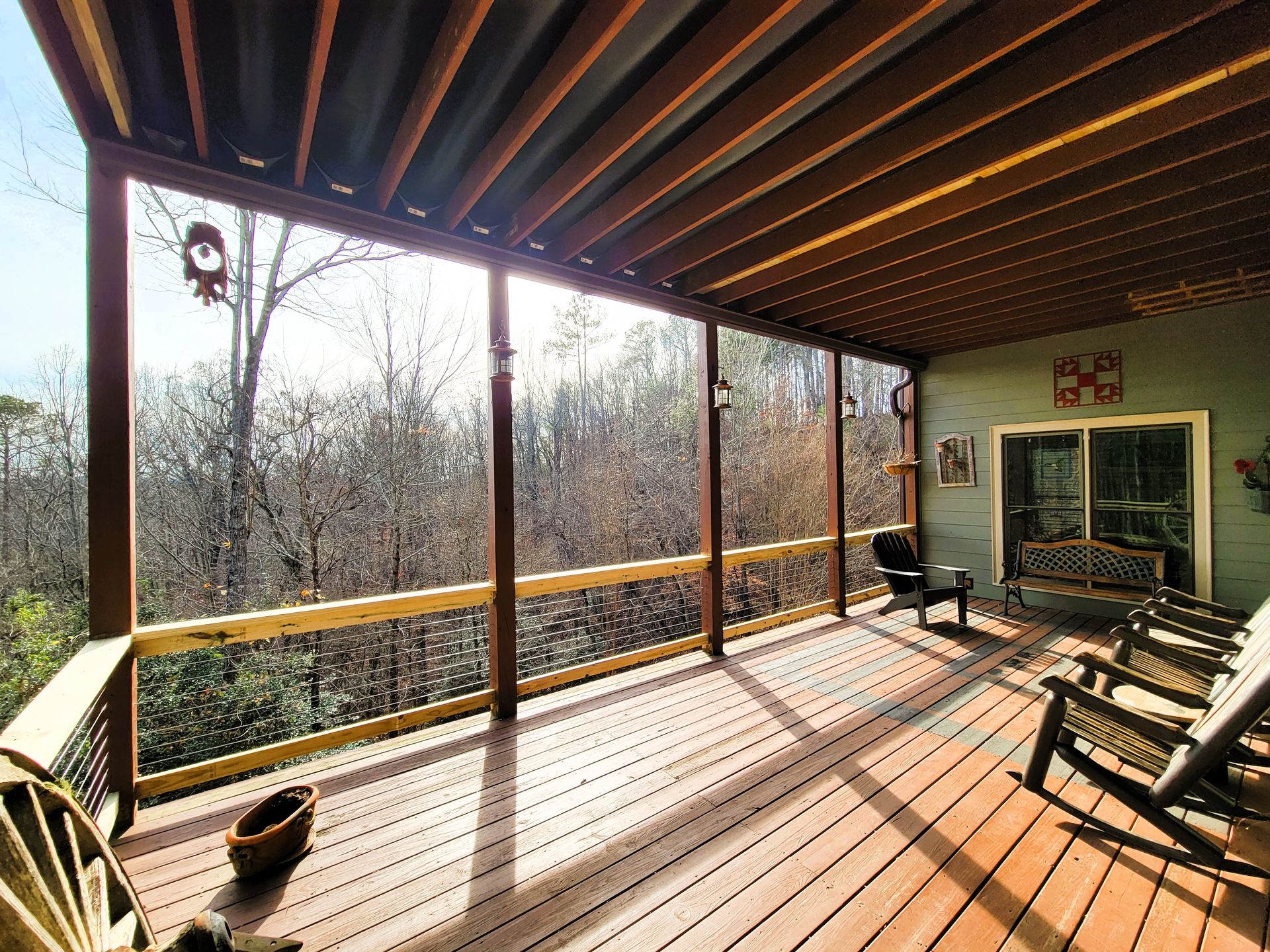 Covered wood deck with cable railing, exposed rafters, and rocking chairs overlooking wooded hillside