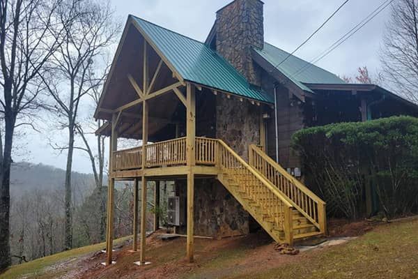 Elevated pressure-treated wood deck with stairs and picket railing on a mountainside cabin with green metal roof