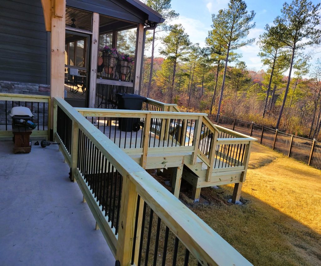 Long pressure-treated accessibility ramp with black metal balusters and a switchback landing running to a raised deck