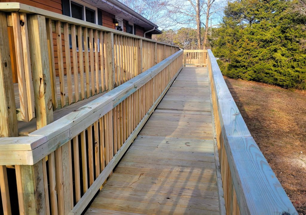 Long pressure-treated accessibility ramp with double handrails and a switchback landing giving step-free access to a ranch home