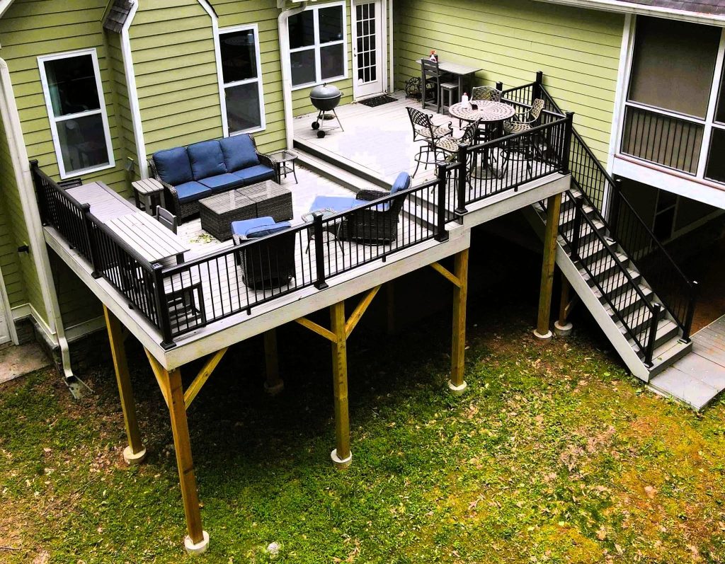 Overhead view of a large elevated deck with black aluminum railing, built-in bench, patio furniture and a long stair run to the lawn