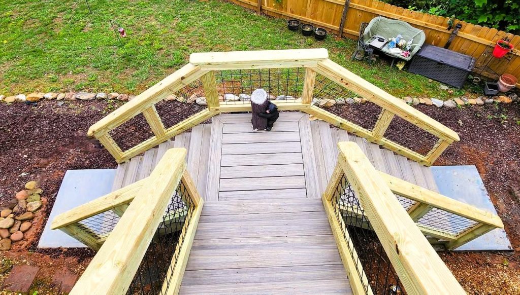 Overhead view of a gray composite deck with angled bay, wire mesh railing and twin stair runs to concrete pads