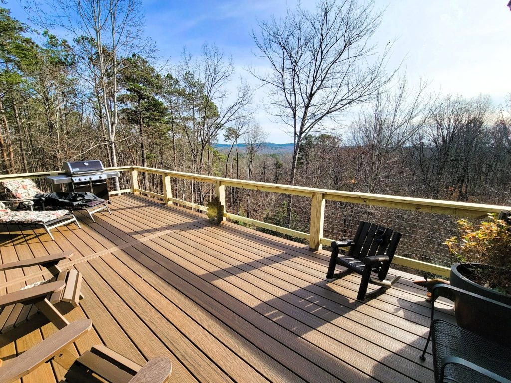 Brown composite deck with pressure-treated cable railing, grill and rocking chair facing a distant blue mountain ridge