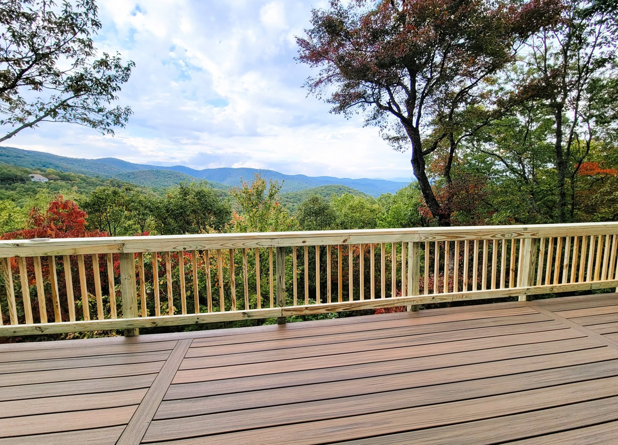 Brown composite deck with pressure-treated baluster railing opening onto layered blue mountain ridges in early autumn