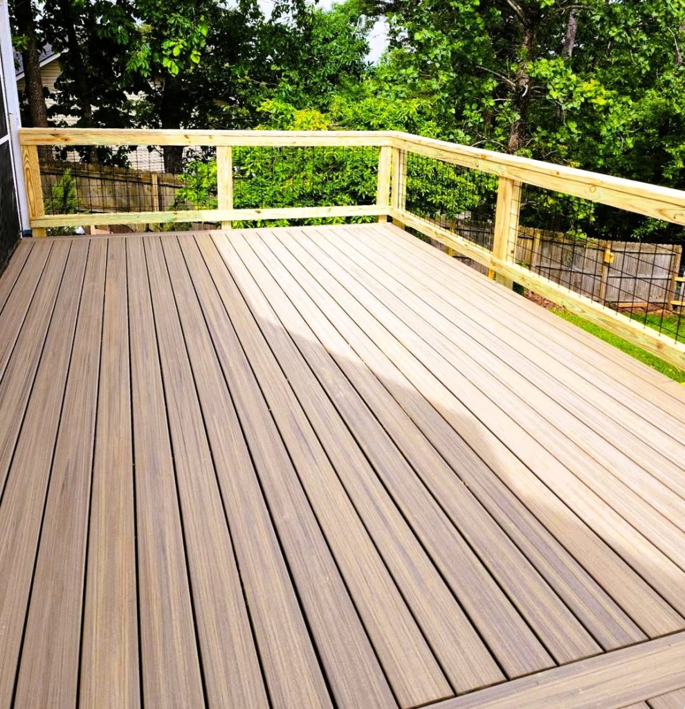 Brown composite deck with pressure-treated wire mesh railing against a privacy fence and mature trees