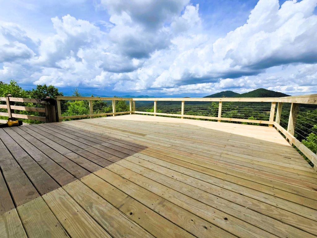 Pressure-treated deck with cable railing opening onto a wide panoramic view of green mountain ridges under cumulus cloud