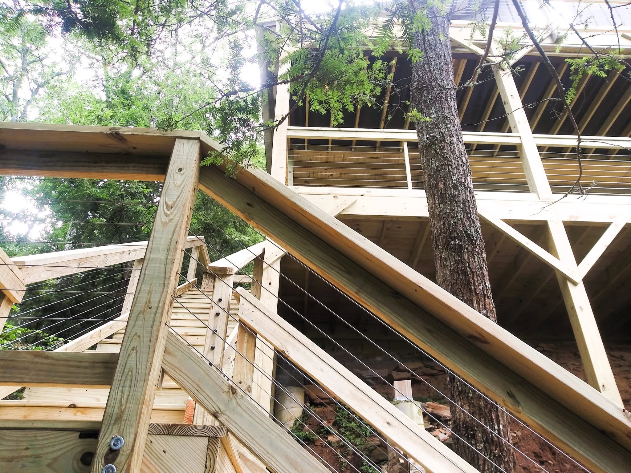 Upward view of a pressure-treated stair run with cable railing and X-braced structural framing beneath an elevated deck