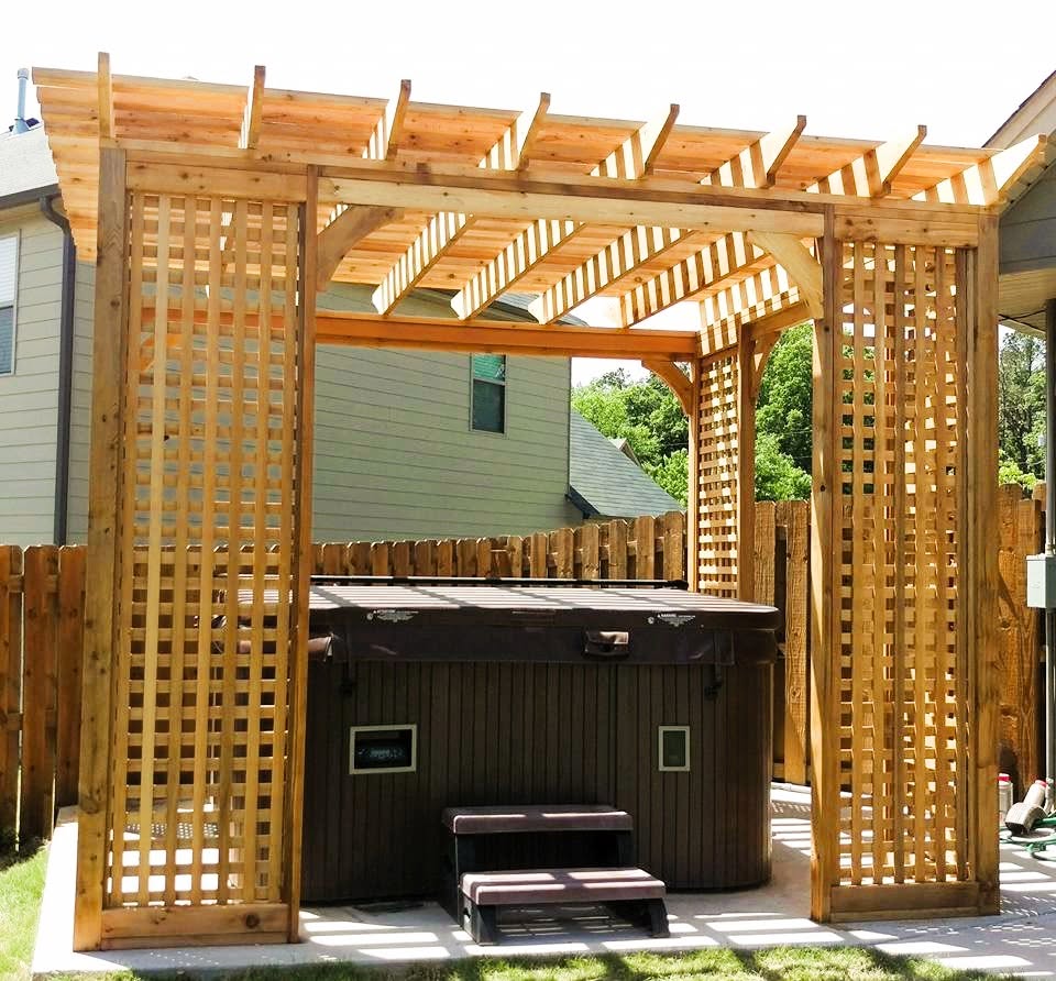 Cedar pergola with lattice privacy screens sheltering a hot tub set on a paver patio beside a wood fence