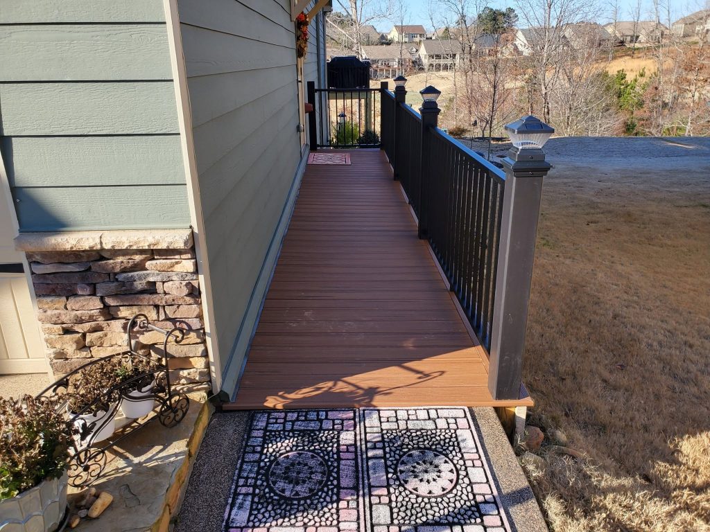 Narrow brown composite walkway deck along the side of a home with black railing and solar-lit post caps