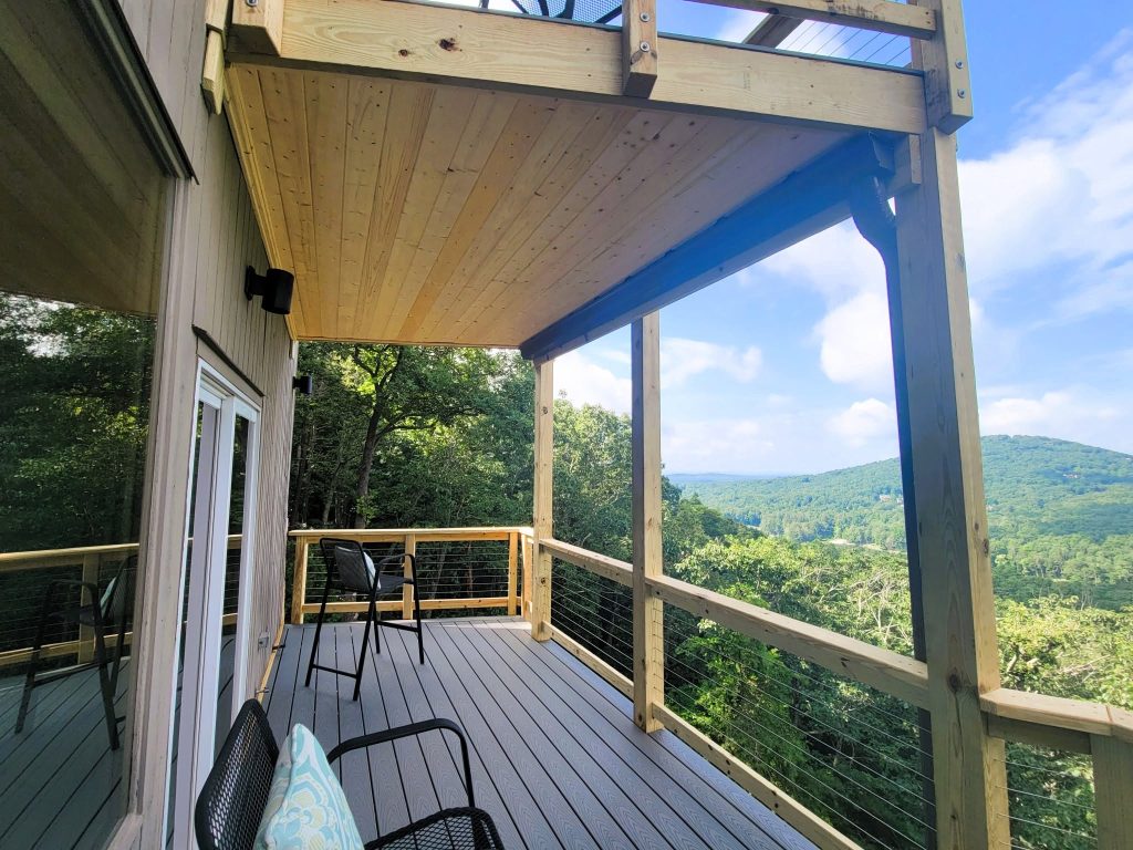 Covered deck with pine tongue-and-groove ceiling, gray Trex composite boards and cable railing facing layered mountain ridges
