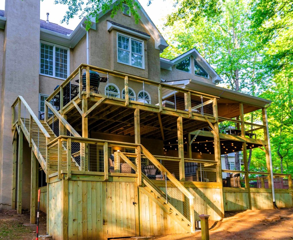 Multi-level cable-railed deck with vertical board skirting and string lights against a stucco home