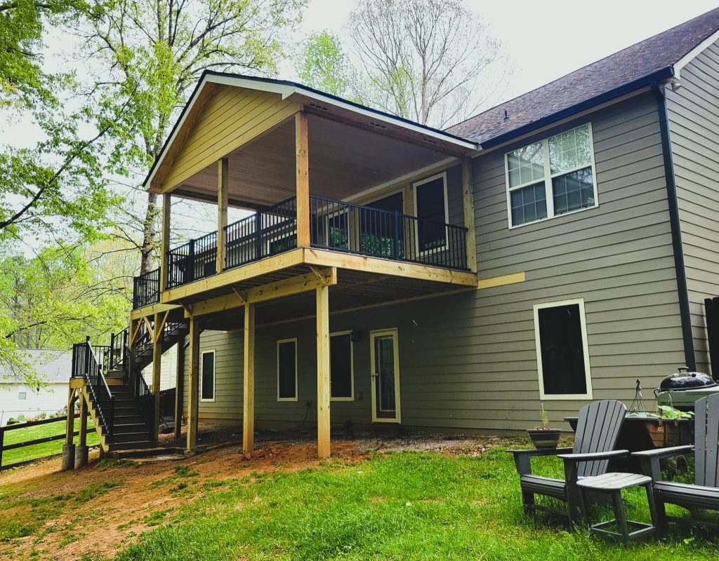 Elevated covered deck with a gable roof, black aluminum railing and a stair run descending to a sloped lawn