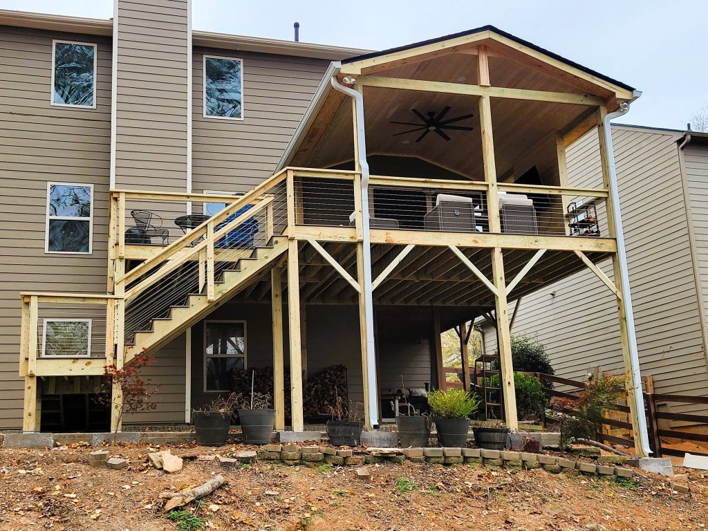 Elevated deck with a gable-roofed covered section, ceiling fan, cable railing and stair run over a firewood store