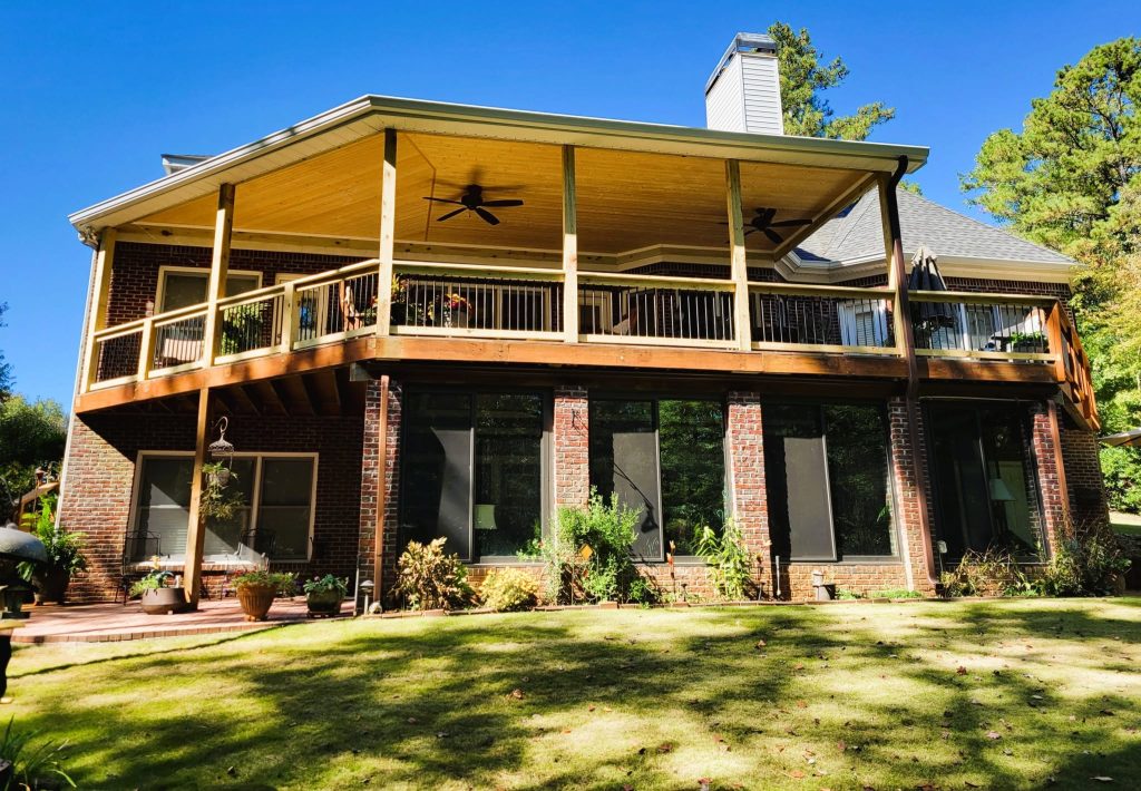 Full-width covered deck with a pine ceiling, two ceiling fans and black baluster railing spanning the rear of a large brick home