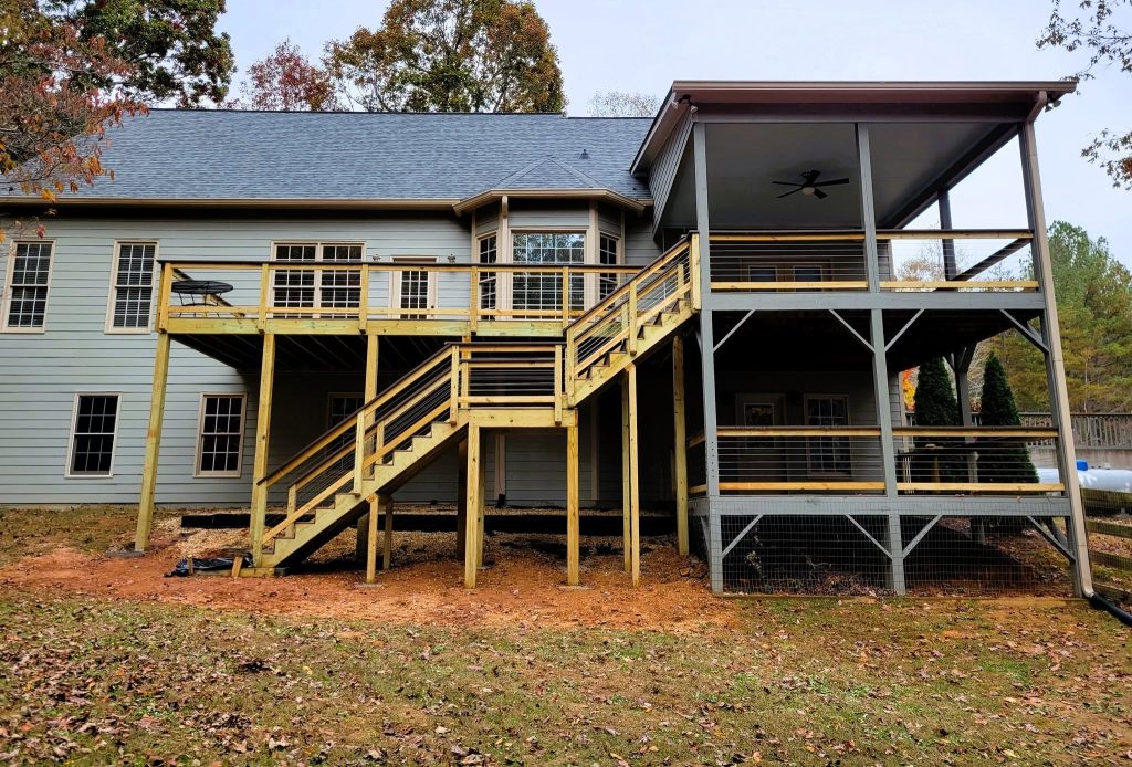 Two-storey rear deck with wood baluster railing above and wire mesh infill screening the covered level below