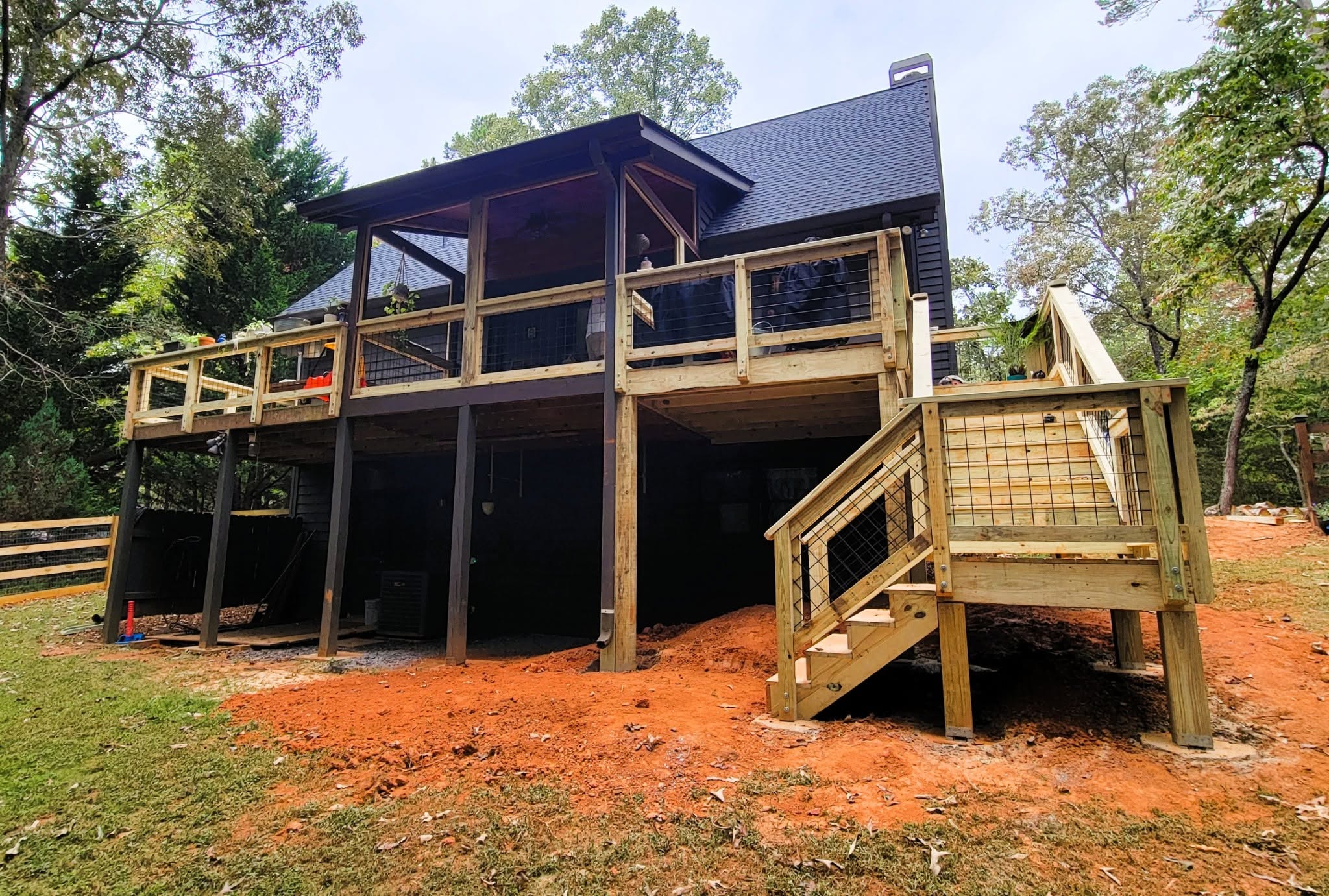 Multi-level deck with hog wire mesh railing under construction on freshly cut red clay ground