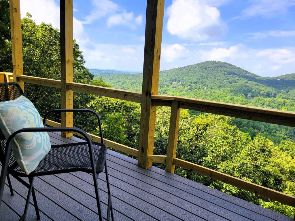 Cable railing and gray composite decking framing a rounded green mountain peak under a blue summer sky