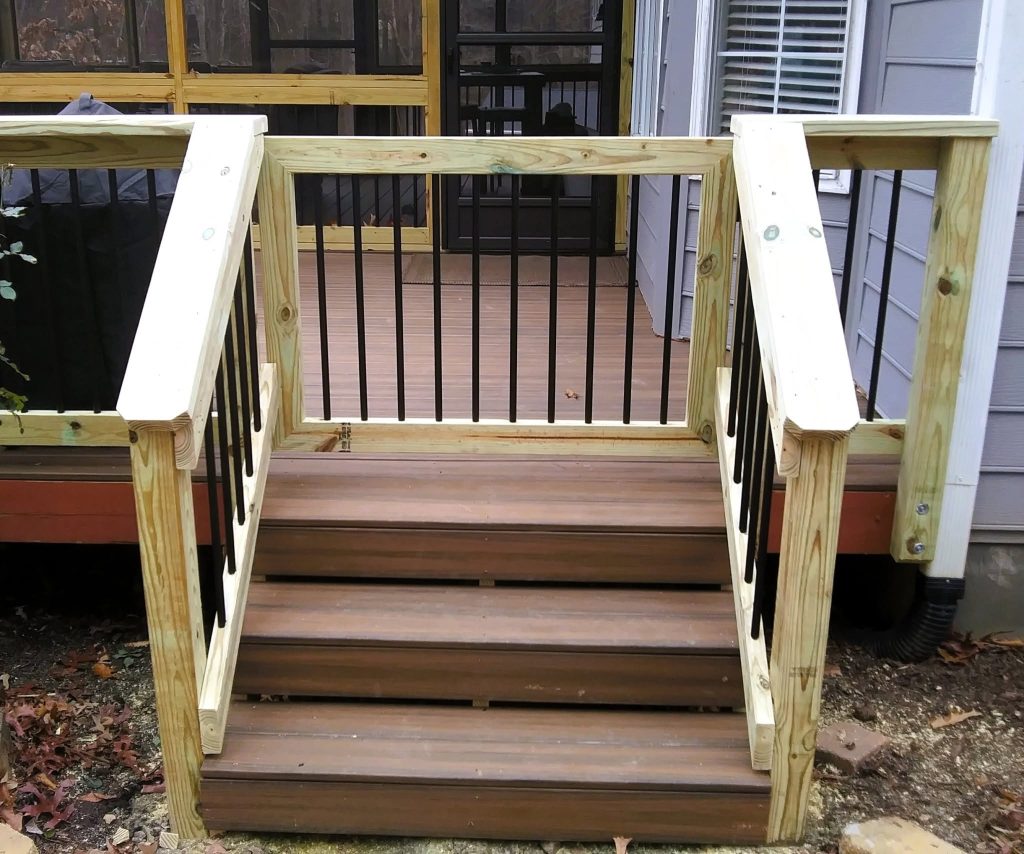 Hinged pressure-treated deck gate with black metal balusters at the head of brown composite steps