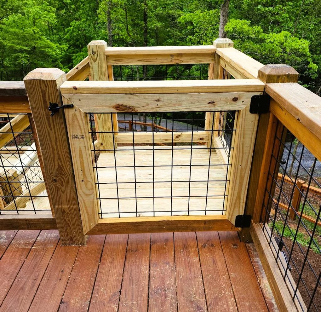 Wire mesh deck gate hung on black hinges with a thumb latch, set into matching mesh railing on stained decking
