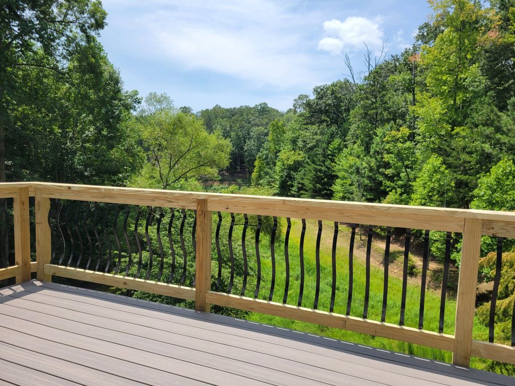Pressure-treated railing with curved black decorative balusters bordering a gray composite deck above a green ravine
