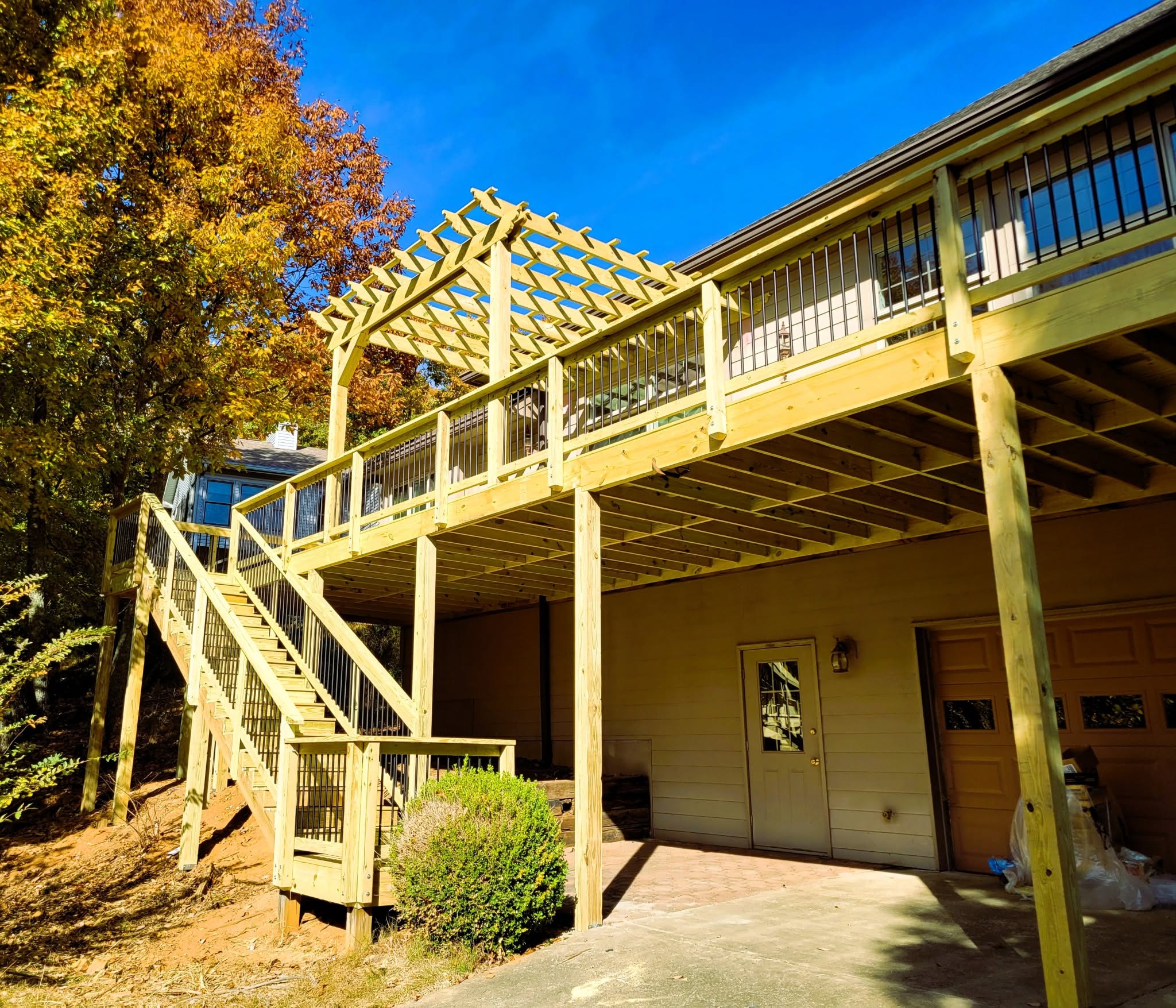 Elevated pressure-treated deck with an attached lattice-top pergola, black aluminum railing and a long stair run in autumn