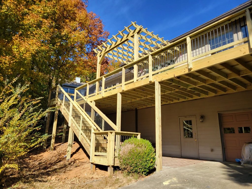 Elevated pressure-treated deck with a lattice-top pergola, black baluster railing and long stair run above a garage in autumn