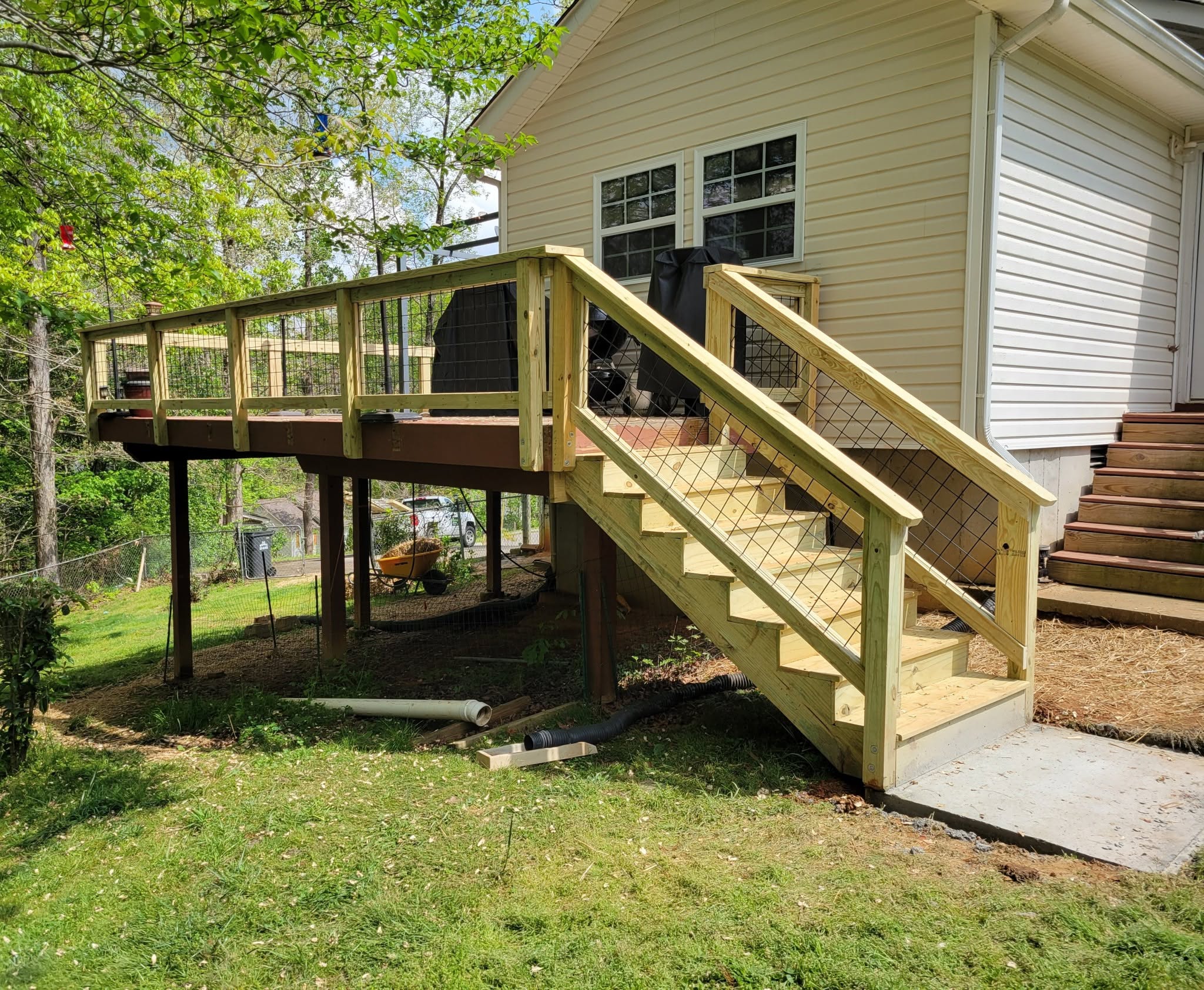 Elevated pressure-treated deck with black wire mesh infill railing carried down the full staircase to a concrete pad