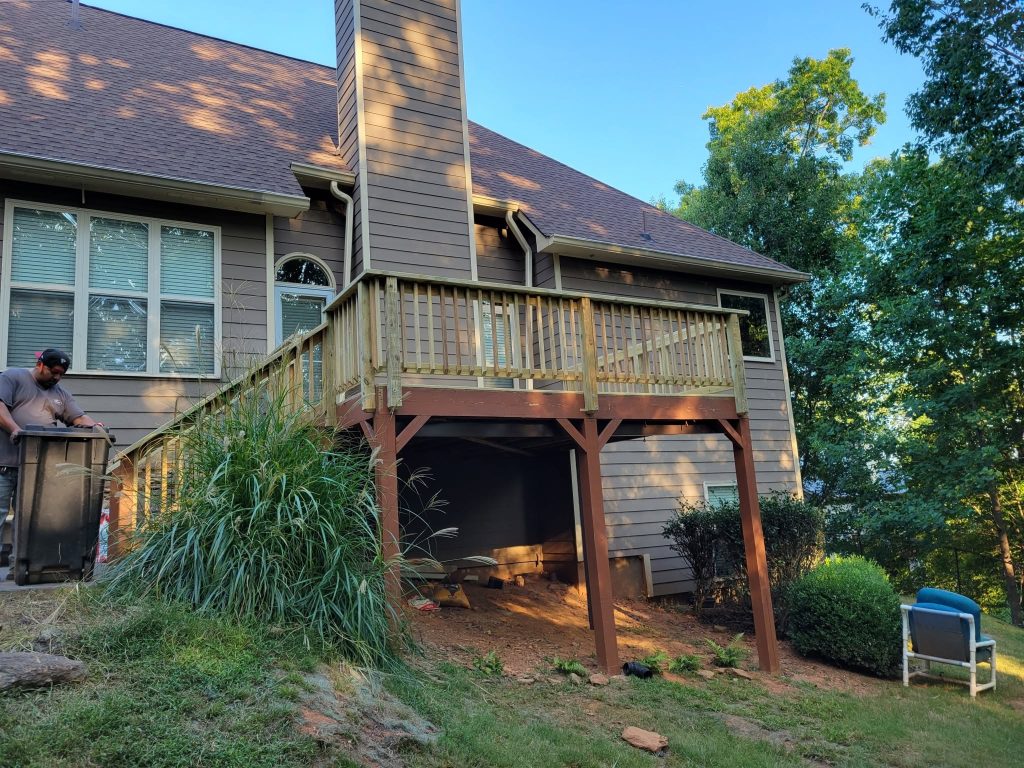 Elevated deck with wood baluster railing on a gray home, a worker at the stair head and grasses below