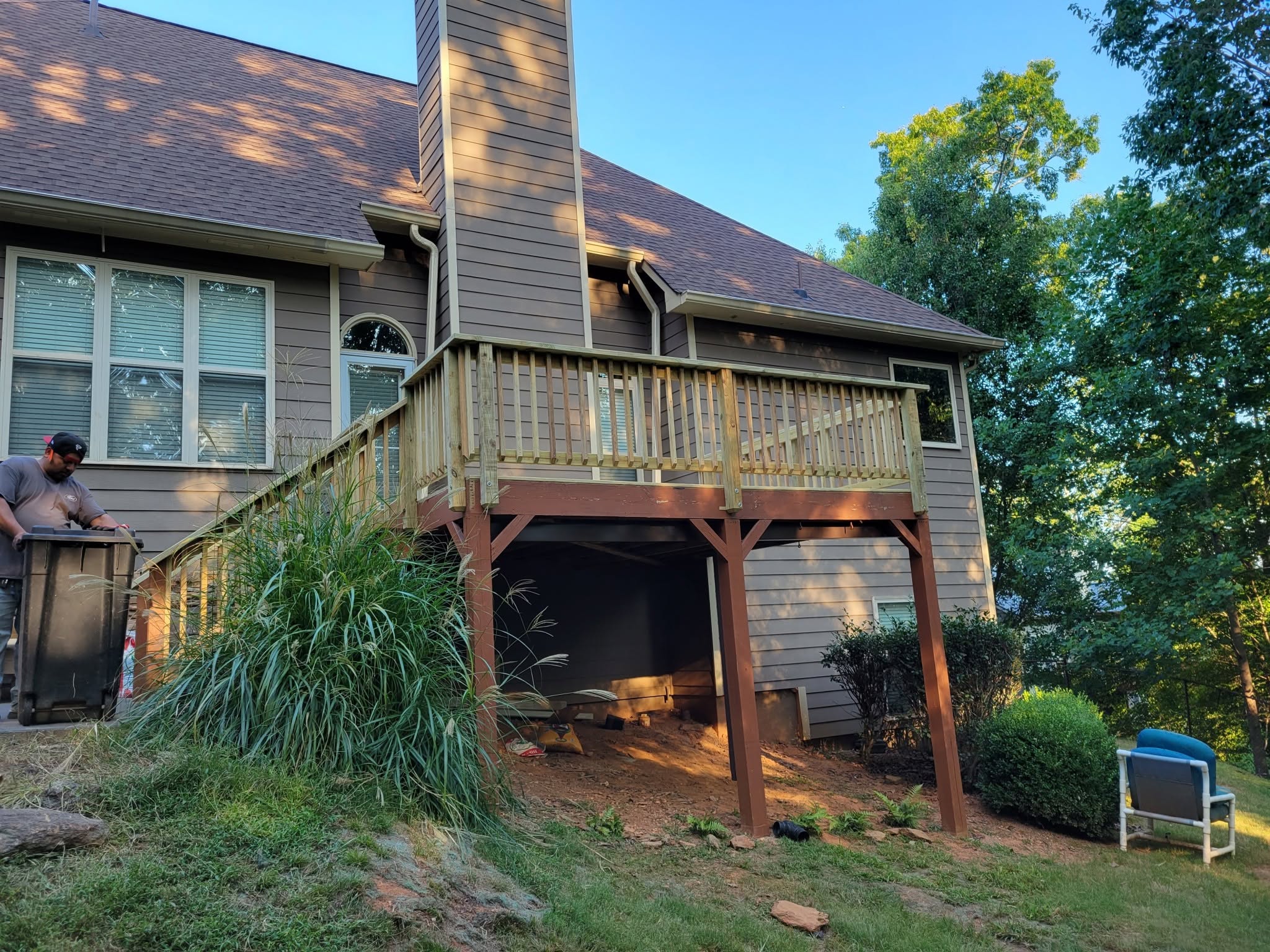 Elevated deck with wood baluster railing on a gray home, a worker at the stair head and grasses below