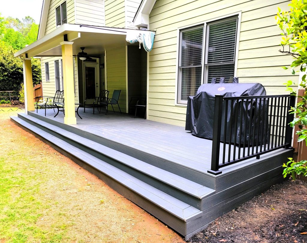 Low gray composite deck with dark fascia banding, black aluminum railing and wide cascading steps beside a covered porch