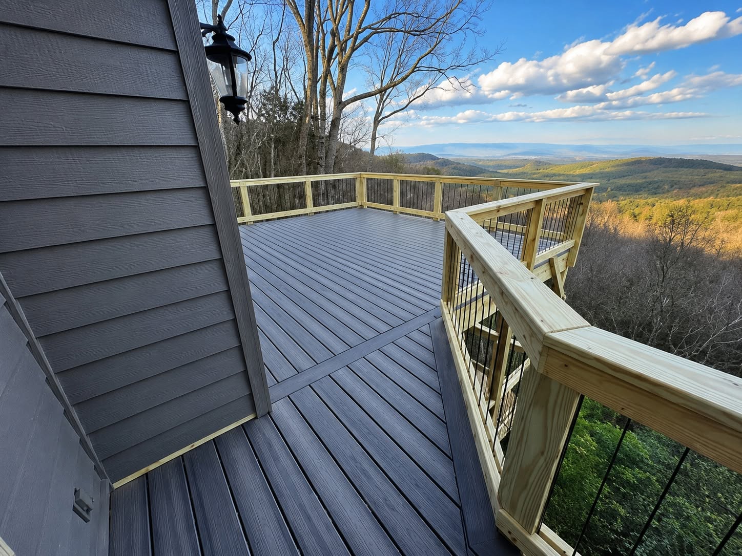Gray composite deck with picture-frame border and pressure-treated cable railing opening onto a wide valley and ridgeline