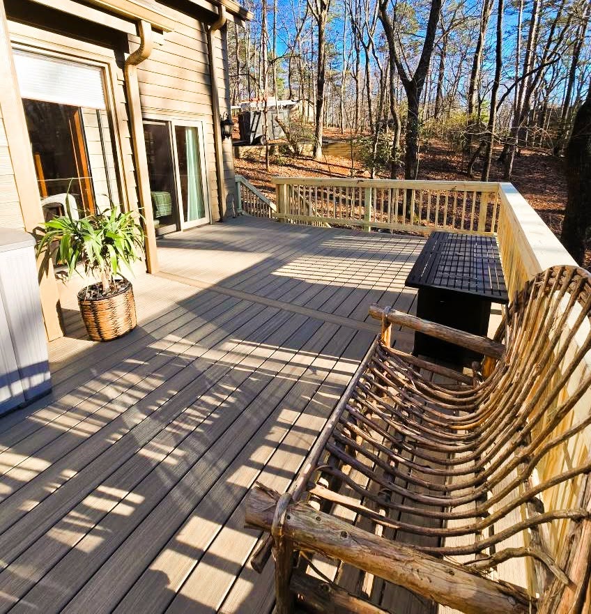 Gray composite deck with directional board banding, a hot tub, built-in bench and pressure-treated railing in winter woods