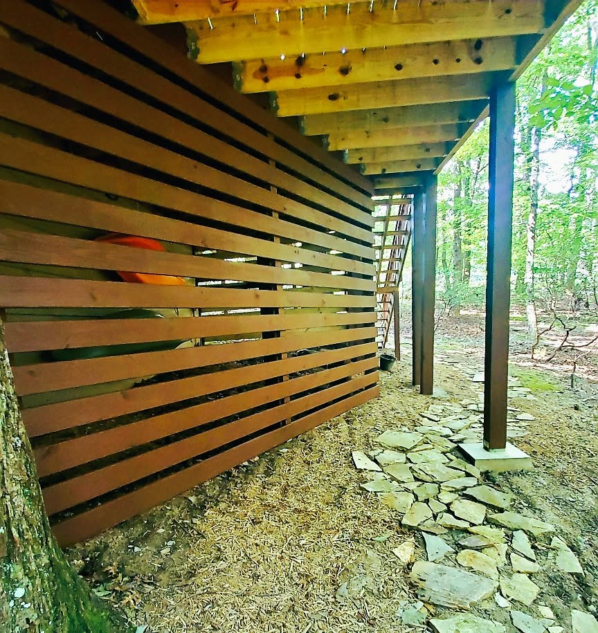 Stained horizontal slat privacy screen enclosing the underside of a deck beside a flagstone path on steel posts