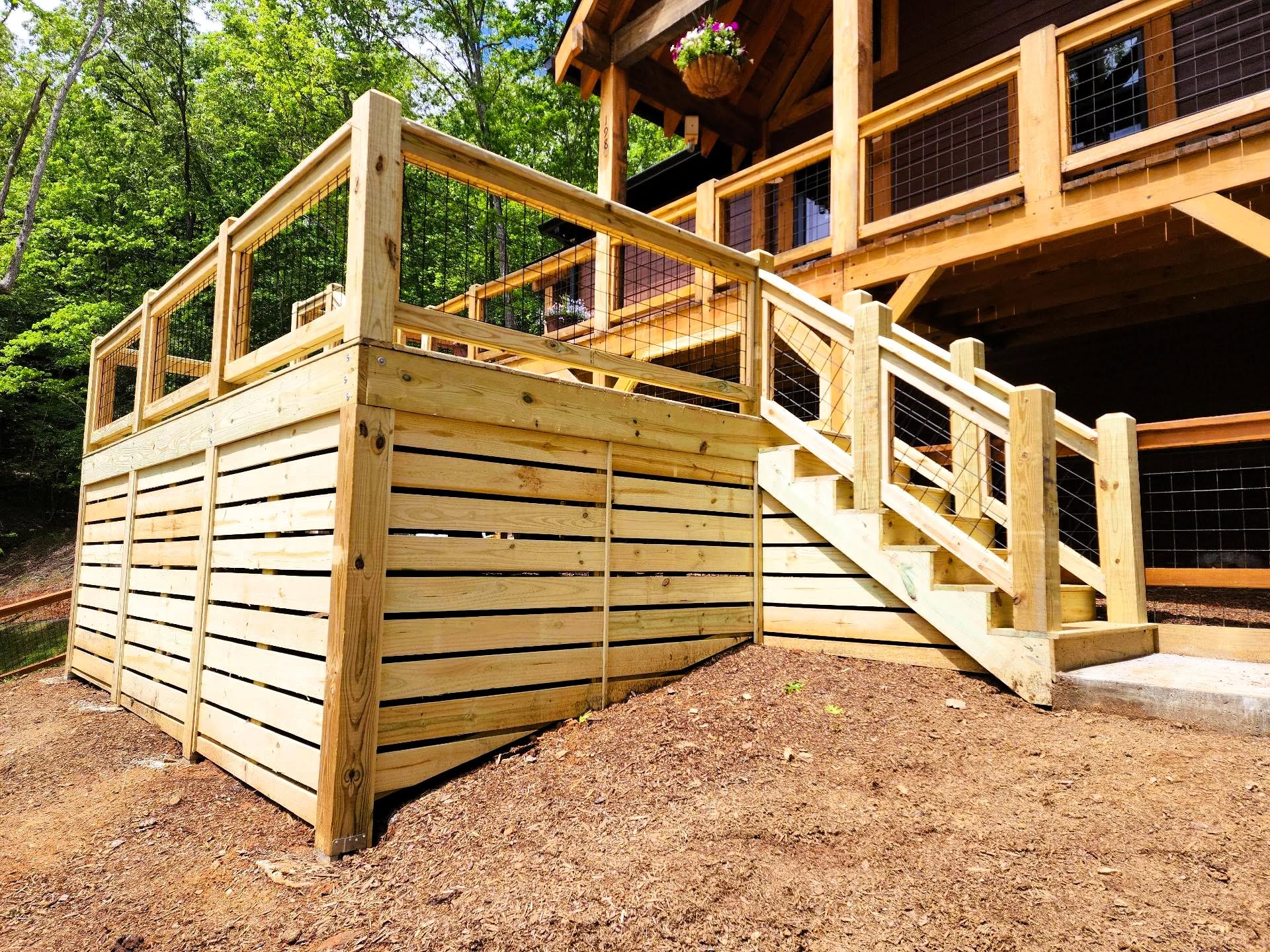 Pressure-treated deck with wire mesh railing above a full run of horizontal slat skirting enclosing the space beneath
