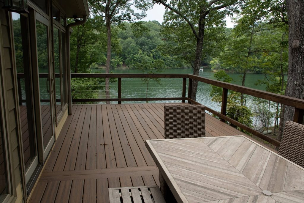 Brown composite deck with dark cable railing overlooking a wooded lake cove with a boat passing in the distance