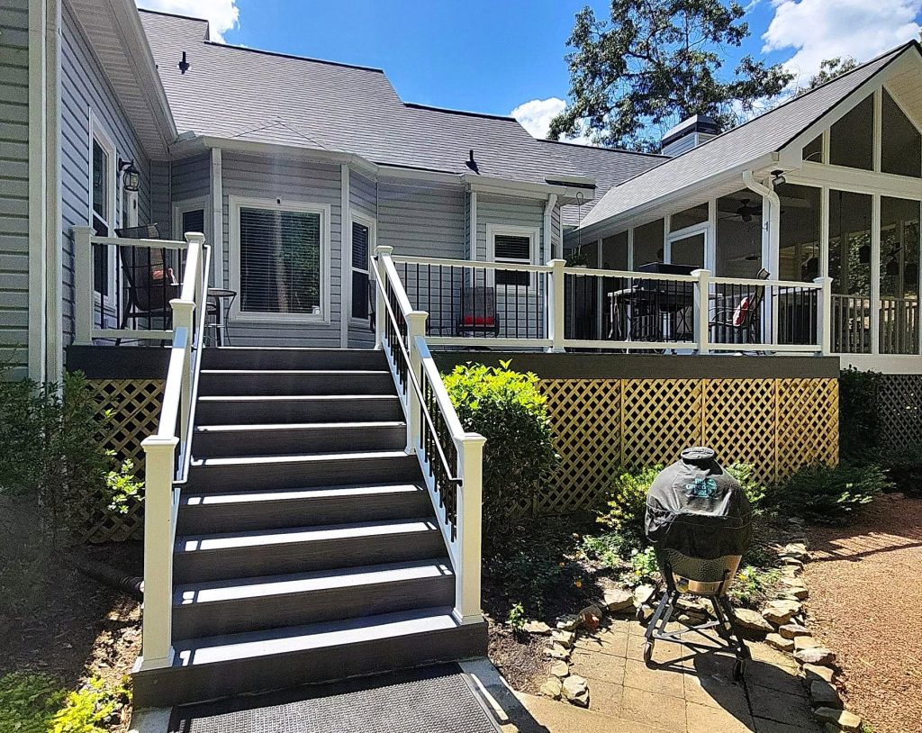 Wide brown composite stair run with white posts and black balusters beside a deck enclosed by fresh lattice skirting