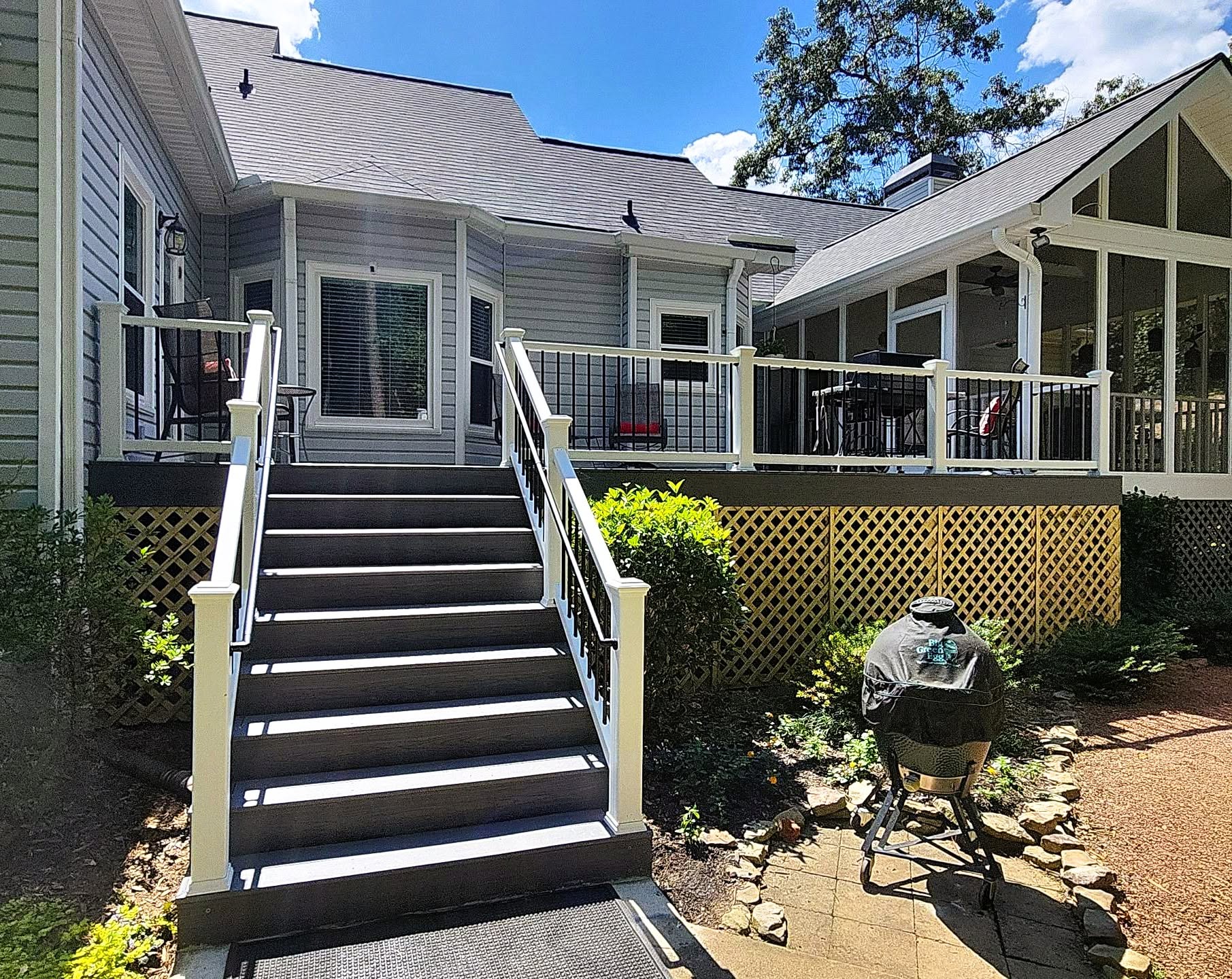 Wide brown composite stair run with white posts and black balusters beside a deck enclosed by fresh lattice skirting