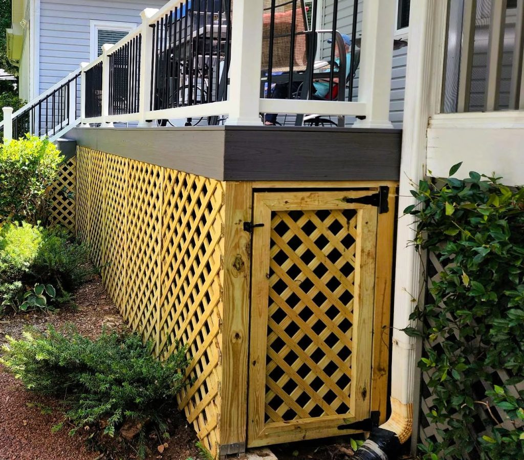 Fresh lattice skirting enclosing the space beneath a composite deck with a framed hinged access door and latch for storage