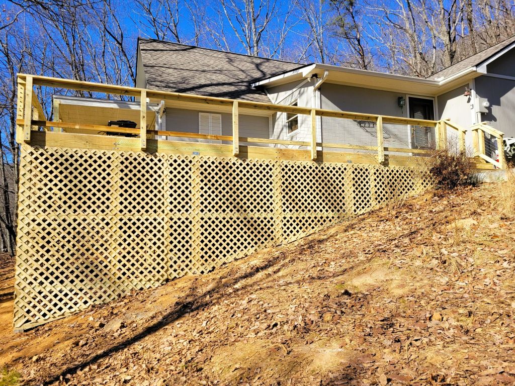 Full run of new lattice skirting enclosing the space beneath a pressure-treated deck with wire mesh railing on a wooded slope
