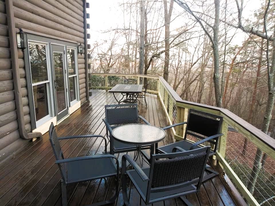 Stained deck with cable railing wrapping a log cabin, patio dining sets under bare winter trees