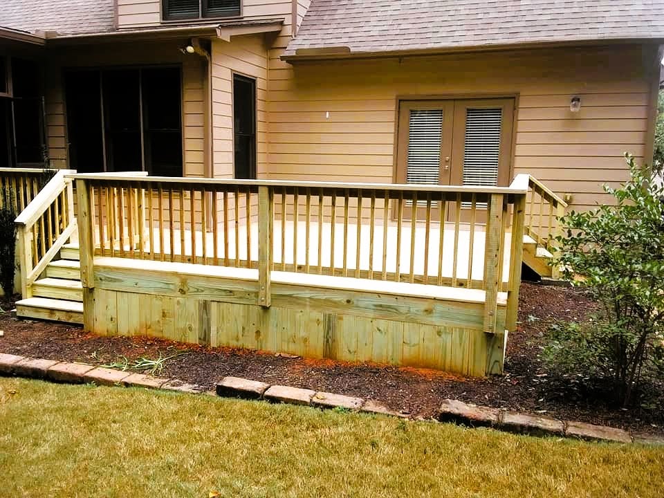 Low pressure-treated deck with wood baluster railing and solid board skirting set into a mulched bed with stone edging