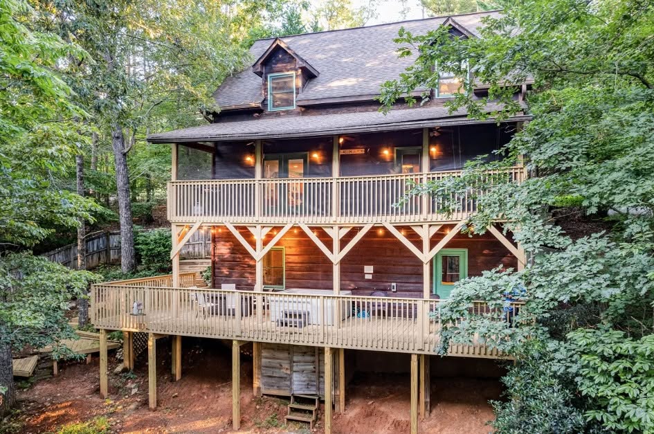 Two-story deck on a wooded cabin with timber knee brackets, warm under-eave lighting and a lower deck level on tall posts
