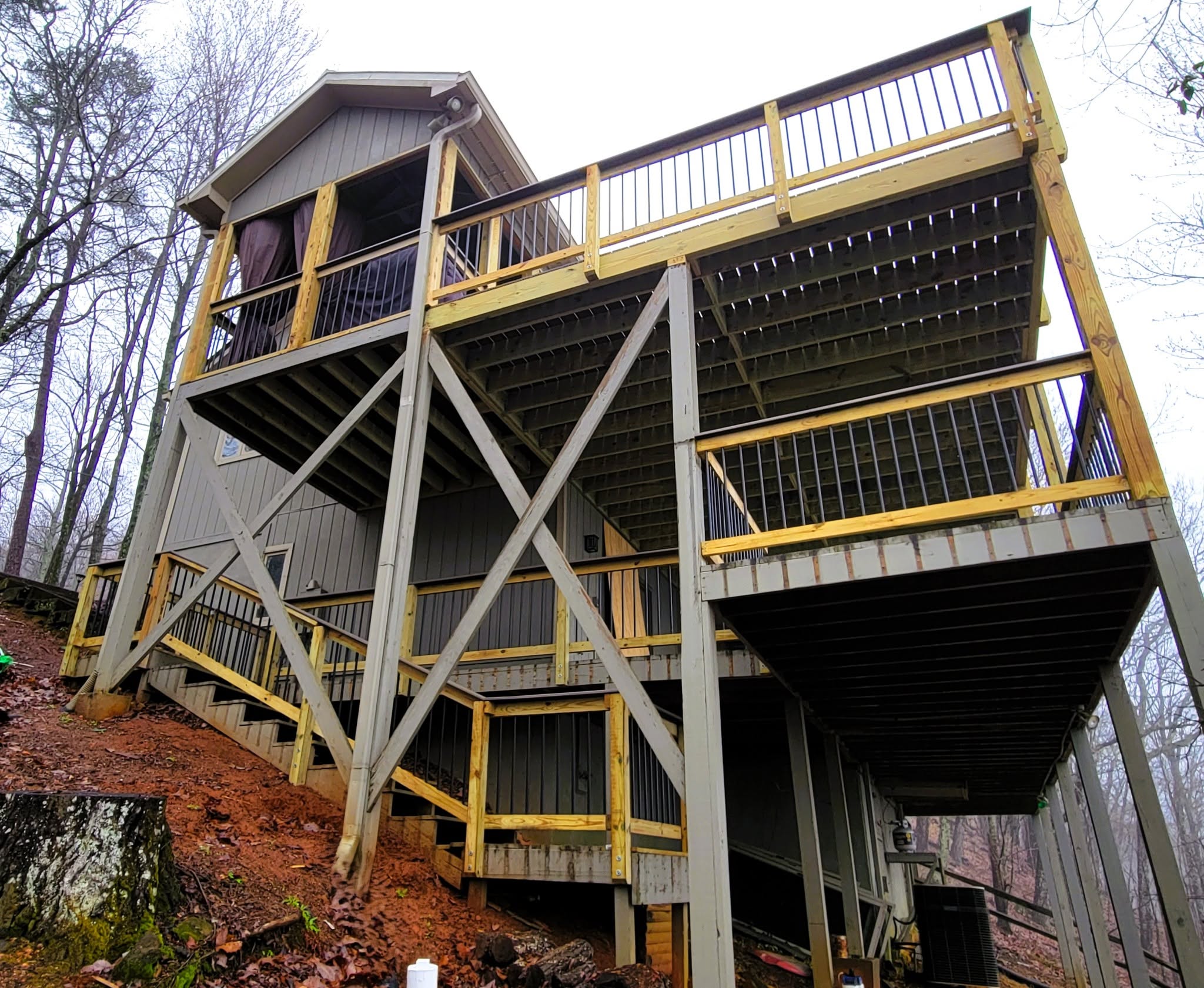 Deck elevated on tall posts with heavy diagonal X-bracing stepping down a steep winter hillside