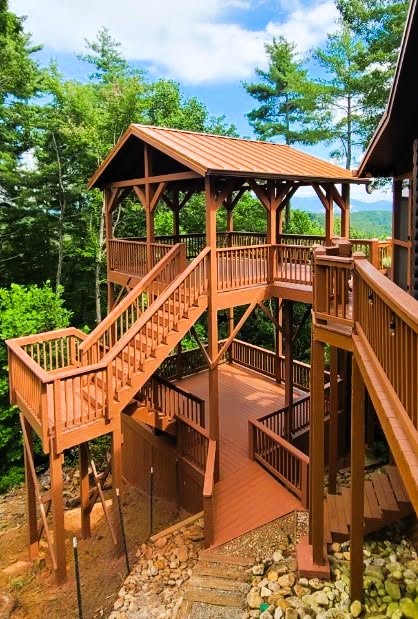 Wrap-around pressure-treated deck with black balusters curving around a cedar-shingled home with a stone chimney