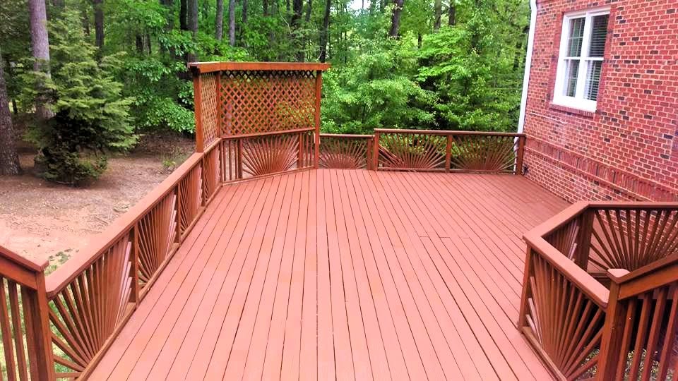 Red-stained wood deck with sunburst corner railing panels and a tall lattice privacy screen beside a brick home