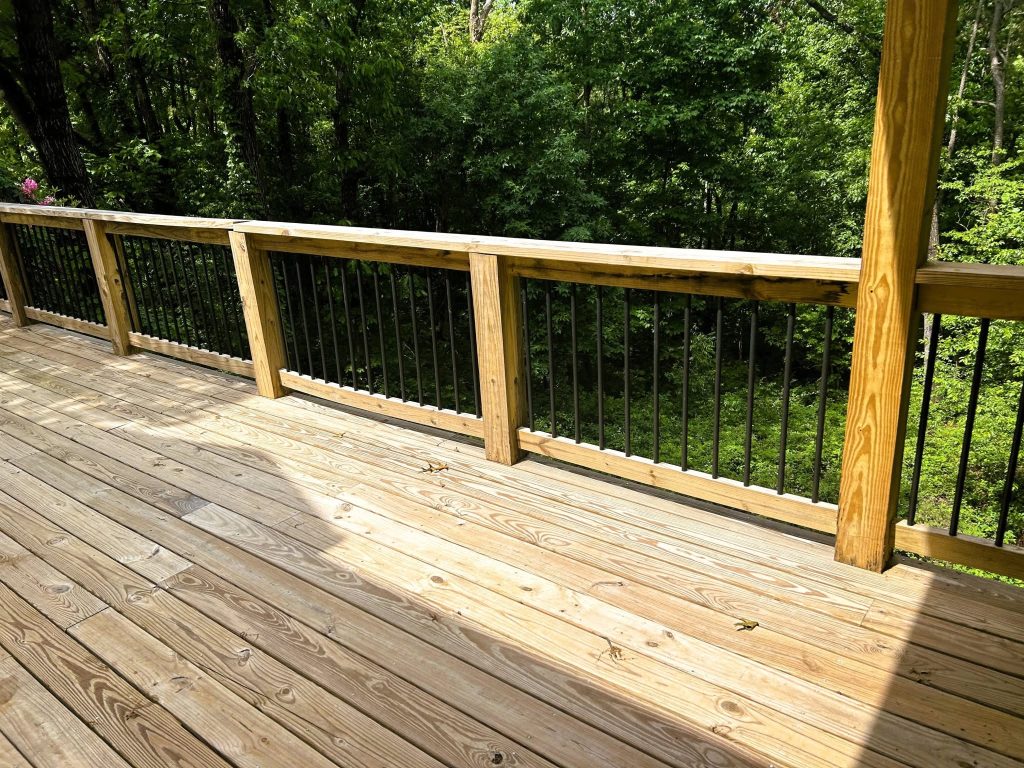 Wide pressure-treated deck with black metal baluster railing in heavy timber frames facing dense summer woods