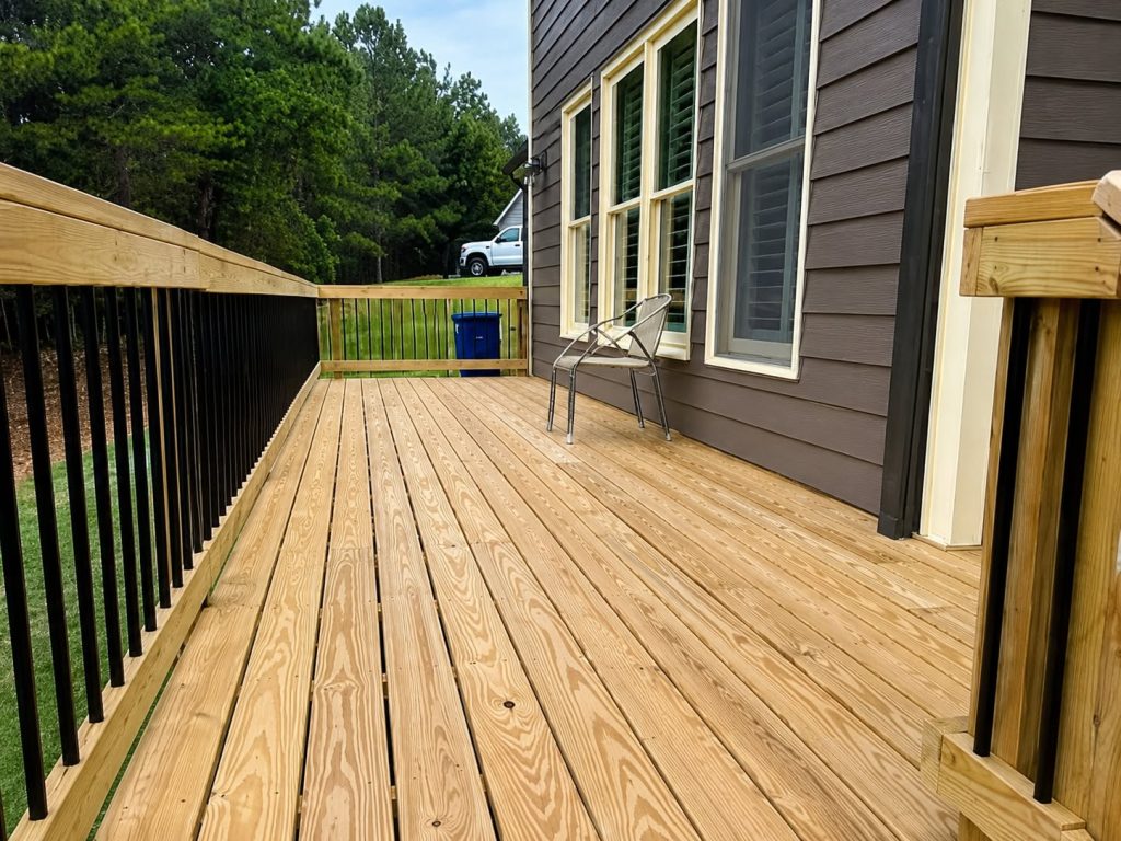 Freshly laid pressure-treated decking with black metal balusters and a wood picket screen panel beside a dark-sided home
