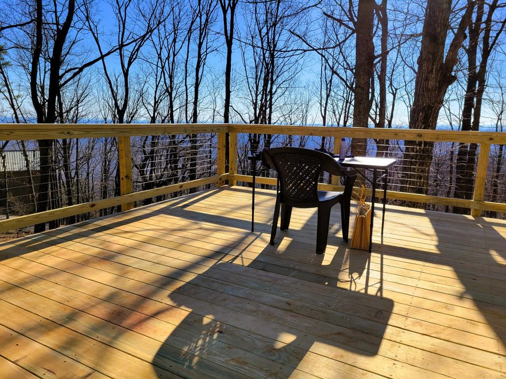 Freshly built pressure-treated deck with cable railing opening onto a winter mountain ridge through bare trees